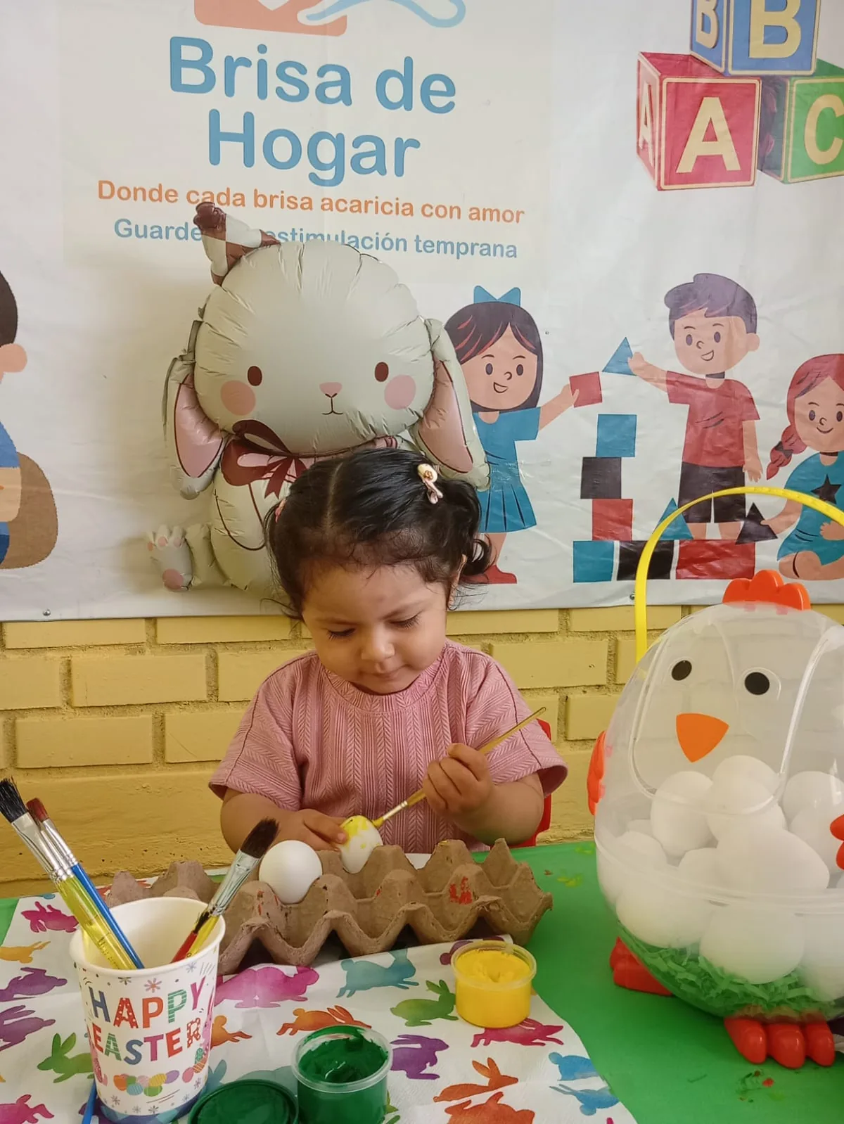 Niña sonriente pintando huevos de Pascua con pinceles — actividad artística en guardería Brisa de Hogar